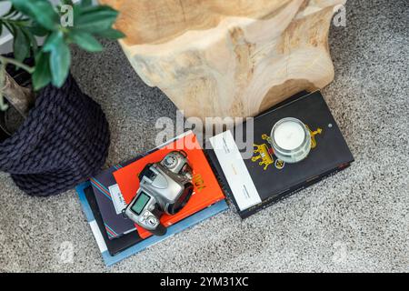 Eine Kamera sitzt auf einem Stapel Bücher und einer Kerze. Die Kamera ist silber und die Bücher rot und schwarz. Die Kerze ist weiß und hat ein Motiv auf mir Stockfoto