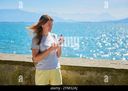 Frau macht an einem sonnigen Tag mit Blick auf die majestätischen Berge malerische Fotos an einem glitzernden See. Idyllische Lage am Seeufer bietet natürliche Schönheit und O Stockfoto