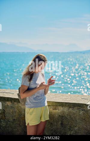 Frau, die an einem sonnigen Tag Fotos an einem glitzernden See mit Panoramablick auf die Berge macht. Frau, die an einem sonnigen Tag malerische Fotos an einem glitzernden See macht Stockfoto