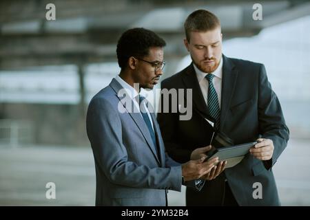 Zwei Geschäftsleute, die sich mit einem Tablet über Geschäftsstrategien unterhalten. Sie sind in formellen Anzügen gekleidet und stehen in modernen Bürobereichen Stockfoto