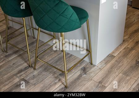 Ein Paar grüne Samtstühle sitzen auf einem Holzboden. Die Stühle stehen neben einer Theke und der Boden ist aus Holz. Die Stühle sind verziert Stockfoto
