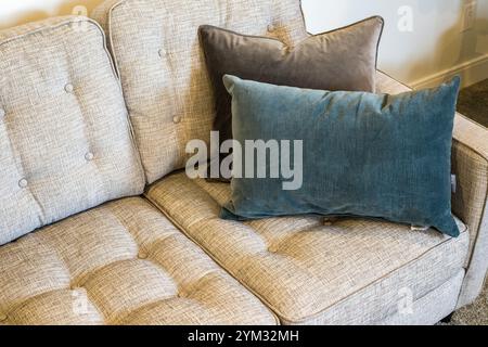 Eine Couch mit zwei Kissen, von denen eins blau ist. Die Liege besteht aus gemustertem Material und hat eine braune Farbe Stockfoto