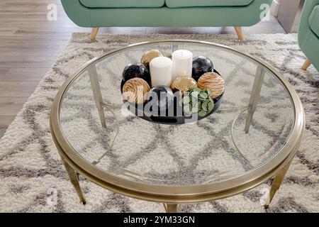 Ein Glastisch mit einer Vase mit Kerzen und ein paar Kugeln darauf. Der Tisch ist von einem Teppich und einer Couch umgeben. Die Szene ist gemütlich und einladend Stockfoto
