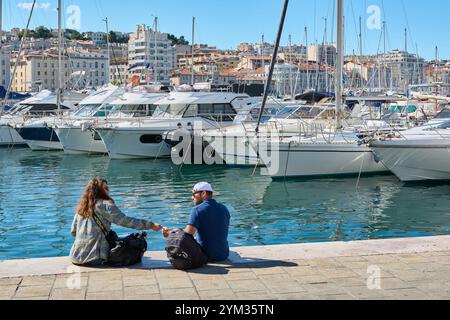 Marseille. Frankreich - 20. November 2024: Zwei junge Menschen unterhalten sich im alten Hafen von Marseille, mit Blick auf Yachten und Gebäude im Hintergrund Stockfoto