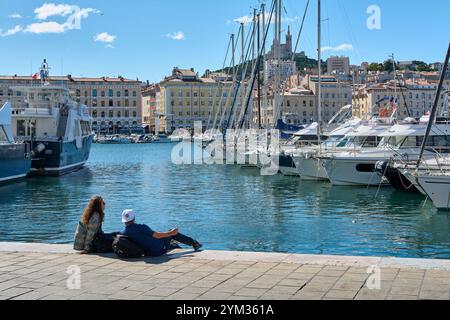 Marseille. Frankreich - 20. November 2024: Friedliche Szene im alten Hafen von Marseille, wo zwei Menschen die maritime Landschaft und die Ankerboote genießen, Stockfoto