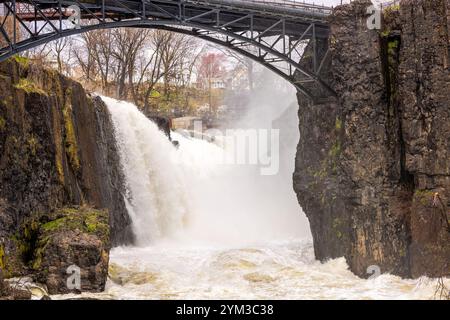 Mächtiger Wasserfall, der zwischen felsigen Klippen mit einer eisernen Brücke über Paterson, New Jersey, kaskadiert. USA. Stockfoto