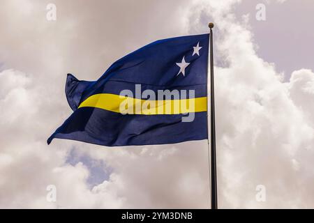 Curacao-Flagge winkt am Fahnenmast gegen bewölkten Himmel an einem luftigen Tag. Stockfoto