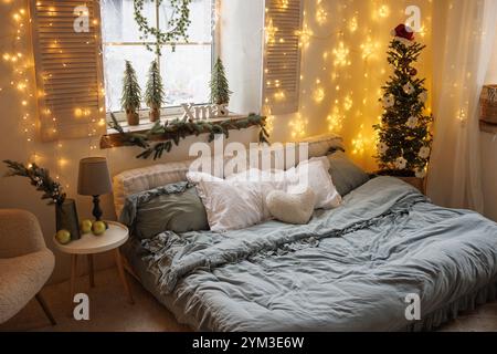 Gemütliches skandinavisches Winterschlafzimmer mit Weihnachtsbeleuchtung, Dekor und Weihnachtsbaum in einer warmen Atmosphäre Stockfoto