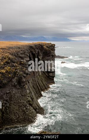 Klippen an der Atlantikküste. Berge am Horizont, teilweise mit Herbstwolken bedeckt. Arnarstapi, Halbinsel Snaefellsnes, Island. Stockfoto