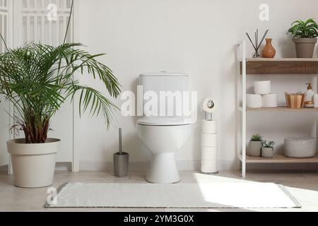 Das Innere der Toilette mit Toilettenschüssel, Regalfach, Zimmerpflanze und Klappschirm in der Nähe der weißen Wand Stockfoto