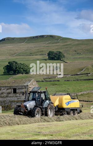 Herstellung großer quadratischer Heuballen auf einer traditionellen Dales Heuwiese, die im Winter mit einem Hurlimann-Traktor und einem New Hol an Vieh verfüttert werden Stockfoto