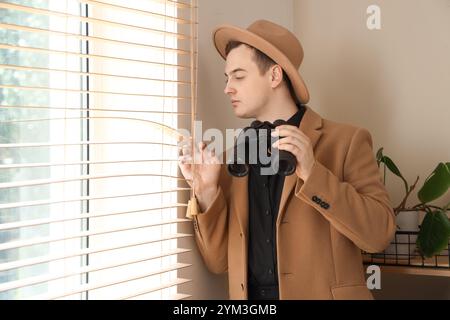 Männlicher Detective mit Fernglas in der Nähe des Fensters im Büro Stockfoto