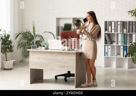 Weibliche Ingenieurin, die mit dem Handy spricht, mit dem Hausmodell und der Windturbine auf dem Tisch im Büro Stockfoto