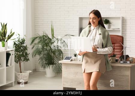 Weibliche Ingenieurin mit Laptop- und Windturbinenmodellen auf dem Tisch im Büro Stockfoto