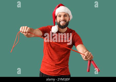 Junger glücklicher Mann im Weihnachtsmann-Hut mit Springseil als Weihnachtsgeschenk auf grünem Hintergrund Stockfoto