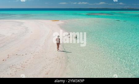 Eine Frau schlendert entlang eines karibischen Sandstrands mit türkisfarbenem Wasser und Palmen im Hintergrund. Die Sonne scheint hell, während sie die malerische tropische Landschaft genießt. Stockfoto