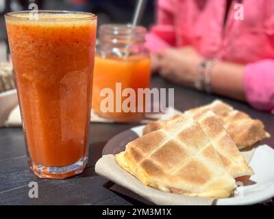 Tisch mit frischen Smoothies und getoasteten Sandwiches im Straßencafé mit nicht erkennbarer reifer Frau im Hintergrund Stockfoto