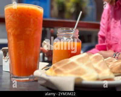 Tisch mit frischen Smoothies und getoasteten Sandwiches im Straßencafé mit nicht erkennbarer reifer Frau im Hintergrund Stockfoto