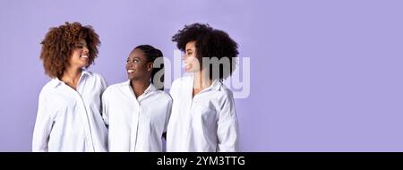 Glückliche drei afroamerikanische Damen, die sich über violettem Hintergrund umarmen Stockfoto
