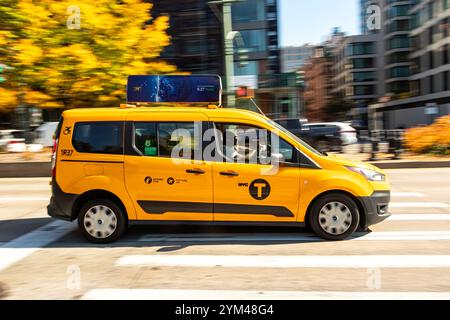 Seitenansicht eines rasanten gelben New yorker Taxibusses, der schnell durch die 5th Avenue fährt, mit verschwommenem Stadtbild und Bäumen im Hintergrund Stockfoto