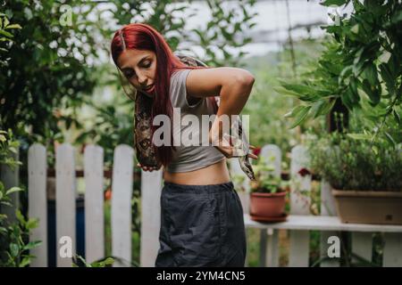 Mädchen mit rotem Haar, das eine große Schlange in einem üppigen Garten hält Stockfoto