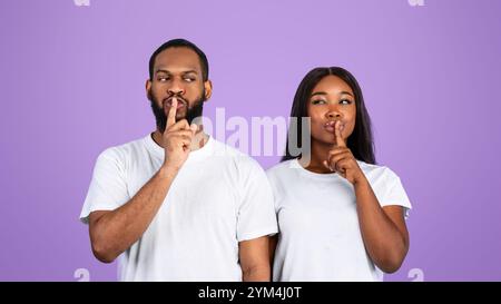 Schwarzes Paar, das Finger auf die Lippen stampft und ein Zeichen für die Stille macht Stockfoto