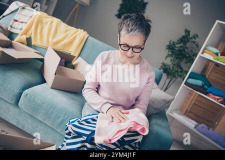 Foto von süßer positiver Dame tragen rosa Sweatshirt, die Spendenkleidung im Innenraum Haus auswählt Stockfoto