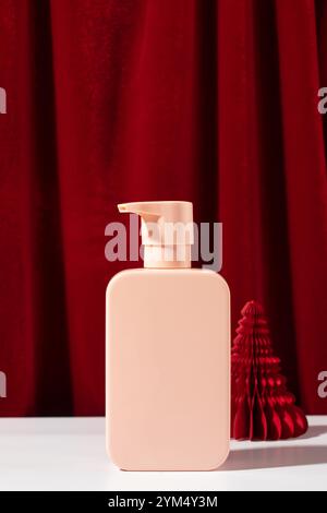 Pinkfarbene Pumpflasche mit Papierweihnachtsbaum in der Nähe des Vorhangs Stockfoto