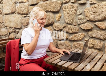 Frau, die im Freien an einem Laptop gearbeitet hat, hat ein Telefongespräch geführt Stockfoto