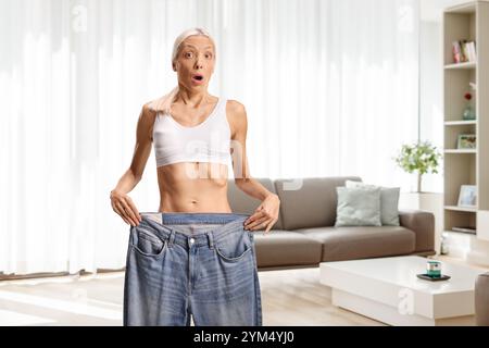 Schockierte junge Frau, die eine große Jeans in einem Zimmer hält Stockfoto