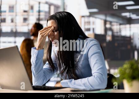 Eine gestresste Geschäftsfrau an ihrem Laptop fühlt den Druck von Projektterminen und emotionalen Belastungen. Die besorgte General Managerin geht mit Müdigkeit und Burnout um, was ihren Arbeitstag zu einer Herausforderung macht. Stockfoto