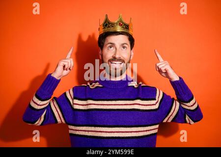 Foto-Porträt des attraktiven jungen Mannes King Point Look Krone gekleidet stilvolle gestreifte lila Kleidung isoliert auf orangefarbenem Hintergrund Stockfoto