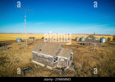 Ein Haus liegt mitten auf einem Feld mit ein paar anderen Häusern und ein paar Metallkörnern. Das Haus ist alt und verlassen Stockfoto