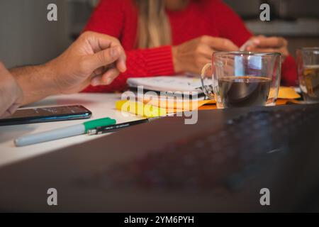 Zwei Personen sitzen an einem Tisch mit einem Laptop und einer Tasse Kaffee. Ehepaar, die Kreditdokumente organisieren . Neues Hauskonzept. Stockfoto