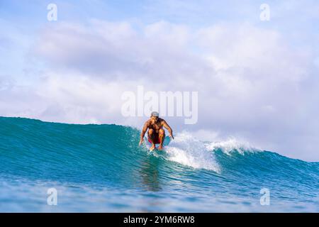 Ein Mann surft auf einer Welle im Ozean. Der Himmel ist bewölkt und das Wasser ist blau Stockfoto