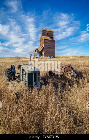 Ein alter Traktor sitzt auf einem Feld neben einem Kornelevator. Der Traktor ist alt und verrostet, und auch das Silo ist alt und verlassen. Die Szene zeigt Stockfoto