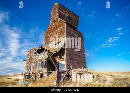 Ein großes altes Backsteingebäude mit vielen kaputten Fenstern. Das Gebäude ist auf einem Feld und der Himmel ist blau Stockfoto