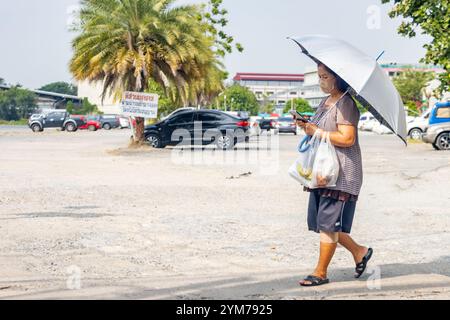 SAMUT PRAKAN, THAILAND, 9. November 2024, ältere Frau, die mit einem Sonnenschirm in der Stadt spaziert Stockfoto