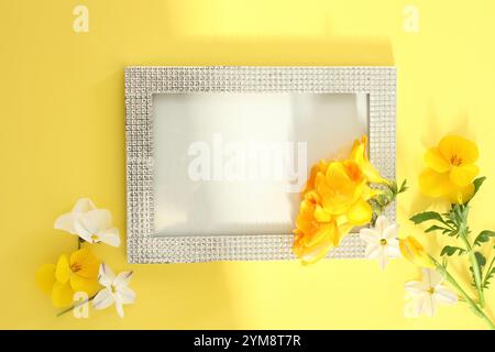 Gelbe Freesie, gelbe Stiefmütterchen und weiße Blüten in einem klaren perlenbesetzten Rahmen auf gelbem Papier (frische Blumen) Stockfoto