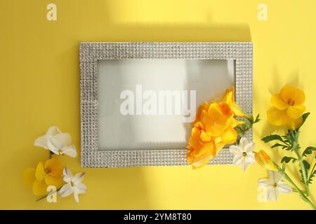 Gelbe Freesie, gelbe Stiefmütterchen und weiße Blüten in einem klaren perlenbesetzten Rahmen auf gelbem Papier (frische Blumen) Stockfoto