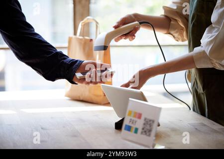 Hände an der Kasse mit einem Smartphone, um eine Zahlung zu tätigen Stockfoto