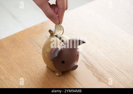 Frau, die Münzen in die Schweinebank in der Hand steckt Stockfoto