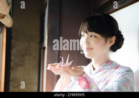 Frau im Kimono mit Origami-Kranichen in Handfläche Stockfoto