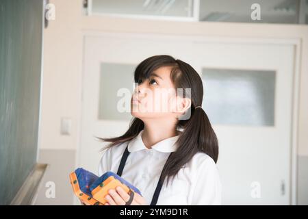 Grundschulmädchen hält Tafelradierer in beiden Händen und schaut nach oben Stockfoto