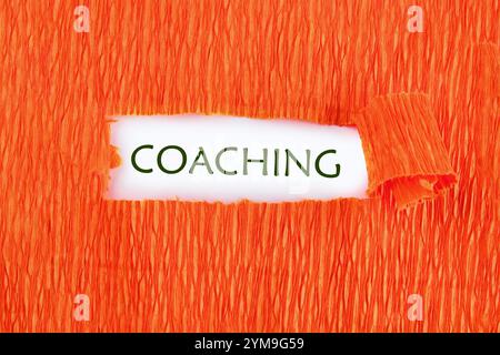 Geschäftskonzept. Der Satz, Text, Wortwahl COACHING ist auf weißem Papier unter orangefarbenem zerrissenem Papier geschrieben. Stockfoto