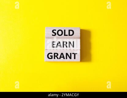 Symbol „Sold Earn Grant“. Verkaufte Konzeptworte verdienen Grant auf Holzblöcke. Schöner gelber Hintergrund. Business und Sold Earn Grant Concept. Kopierbereich. Stockfoto