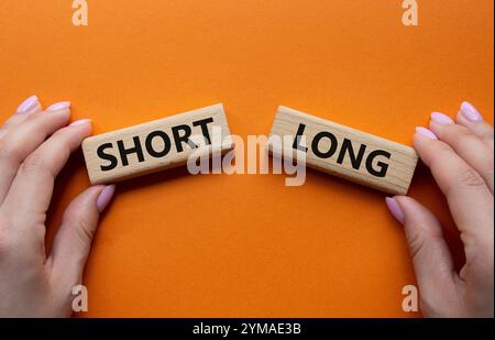 Symbol kurz vs lang. Konzeptwort kurz vs lang auf Holzblöcken. Geschäftsmann Hand. Wunderschöner orangefarbener Hintergrund. Business und kurz- vs Langkonzept. Stockfoto
