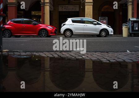 bologna, Italien. 9. Oktober 2024: Rote und weiße Autos parken auf der Straße, mit Reflexion des berühmten Portikus Stockfoto