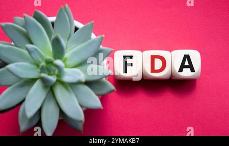 FDA – Symbol für die Arzneimittelverwaltung. Holzwürfel mit Wort FDA. Schöner roter Hintergrund mit saftiger Pflanze. Medizinische und Food Drug Administration Stockfoto