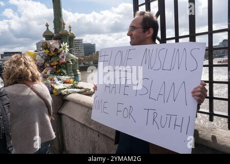 April. Zehn Tage nach dem Terroranschlag in Westminster steht ein Mann in der Nähe der Blumen für die Opfer um einen Lampenstandard auf der Waterloo Bridge mit einem Poster „#Love Muslims Hate Islam Time for Truth!“ Stockfoto